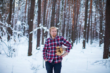 a man in a checkered shirt carries a pile of firewood in the winter forest