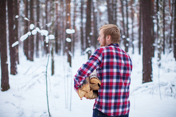 a man in a checkered shirt carries a pile of firewood in the winter forest