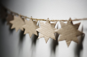 Simple Christmas cardboard stars garland decoration on white wall background.