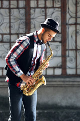 Fototapeta na wymiar Young man plays saxophone on urban background
