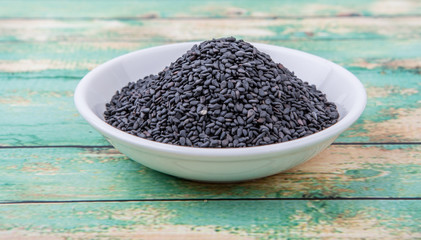 Black sesame seed in white bowl over wooden background