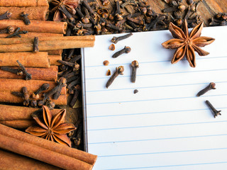 blank notebook, cinnamon sticks, cloves and  star anise on wooden background