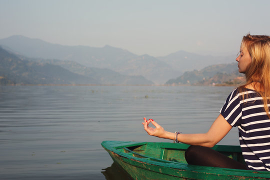 Girl practicing yoga meditation on the shore of mountain lake in  boat
