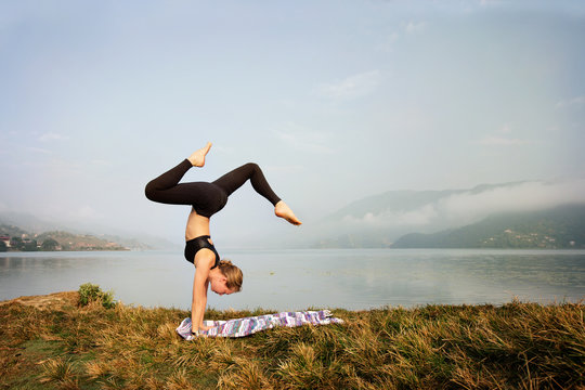 Young woman doing  yoga exercise in morning on  shore of mountain lake. Handstand. Fitness and gymnastic sport outdoor