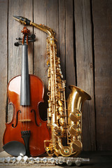 Naklejka premium Musical instruments: saxophone, violin and flute with notes on wooden background