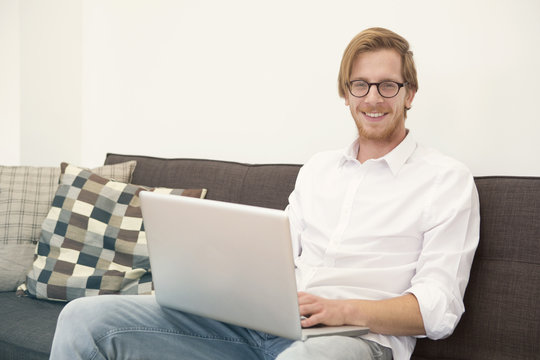 young man sitting on couch with laptop and smiles