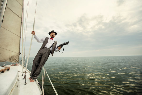 Gangster mafia man on yacht boat with gun weapons in hand. Sea background, Escape