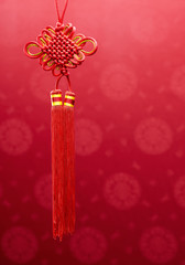Chinese knot hanging decoration over red fabric with oriental motifs background