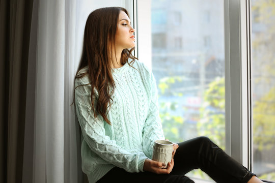 Pretty woman sitting on the window board with cup of coffee