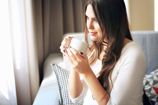 Beautiful woman relaxing on sofa in the room with cup of coffee