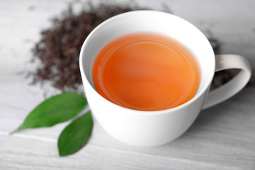 Ceramic cup of tea with scattered tea leaves around on light wooden background