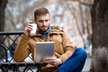 Handsome consentrated bearded man using tablet in open air cafe
