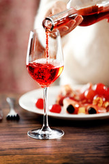 Young woman pouring pink wine into glass on the table