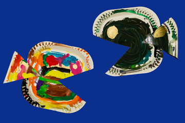 Fish made from paper plates and painted by child. Fish crafted by a child isolated against a blue background

