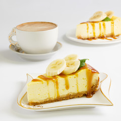 Slice of cheesecake with banana and caramel sauce, cup of coffee on the white background