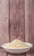 White sesame seed in white bowl over wooden background
