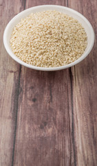 White sesame seed in white bowl over wooden background