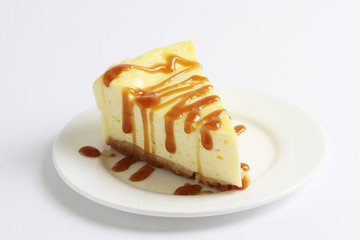 Slice of cheesecake topped with caramel sauce on plate on white table, close up