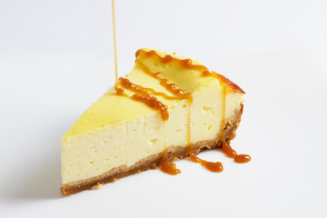 Piece of cheesecake pour a thin stream of caramel sauce/ Piece of cheesecake isolated