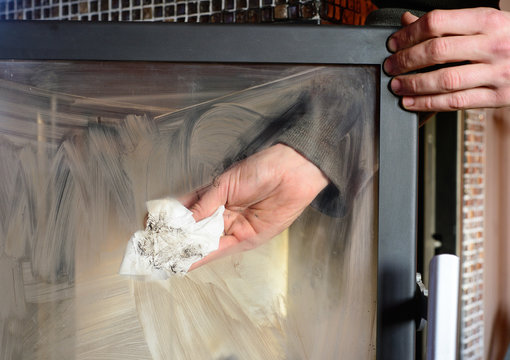 man wipes the dirty glass of fireplace