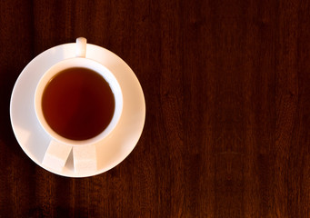 White Cup of tea, a saucer of sugar cubes, a dark wooden background
