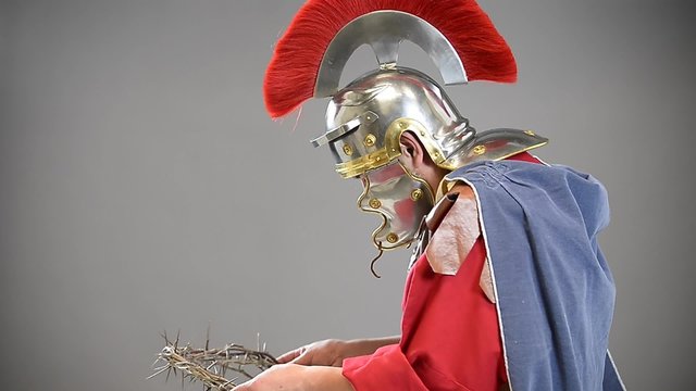 Roman soldier holding crown of thorns over gray background