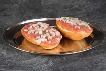 Zwei Brötchenhälften auf einem Silbertablett. Belegt mit Mett und Zwiebeln. Gewürzt mit Pfeffer und Salz.