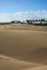 Maspalomas next to dunes under blue sky with few clouds /  Large sandy dunes in a wide dessert in south of Gran Canaria