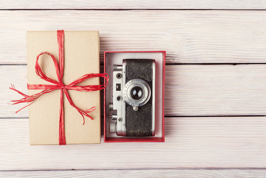 Gift box with retro camera over light wooden background