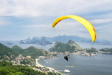 Bright yellow hang glider flying over the mountainous skyline of the city skyline from the Parque...