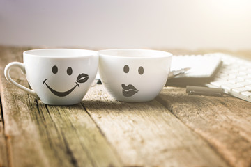 Two cups of coffee with slimey and kiss face on wooden table wit