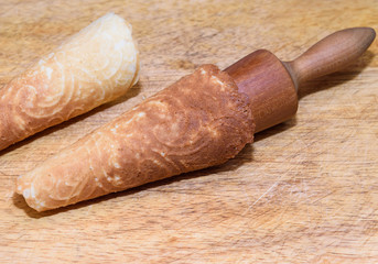 Finished Krumkake cookie on a rolling cone, sitting on a cutting board
