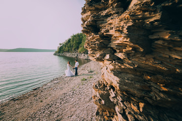 beautiful gorgeous blonde bride and stylish groom holding hands, on the background of a sea