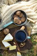 Mug with red wine, delicious cheese and nuts on wooden board outdoors - picnic theme