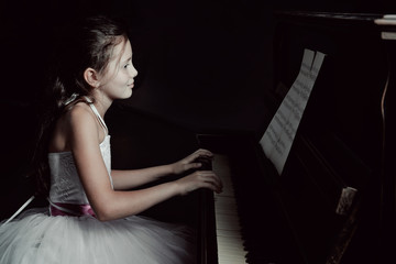 Cute little princess girl plays piano in the dark room