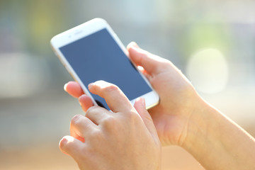 Female hands holding a mobile phone outdoors, on blurred background