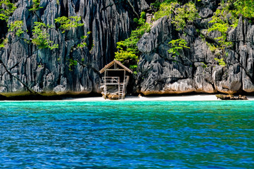 Lonely wooden bamboo house on stilts at a small hidden beach of rocky island