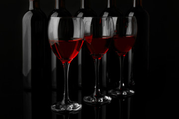 Wine glasses against bottles in a row on black background, close up