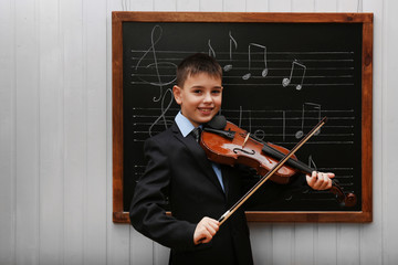 Young cute schoolboy playing the violin the blackboard with musical notes
