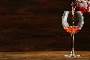 Rose wine pouring in glass on wooden background