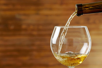 White wine pouring in glass on wooden background