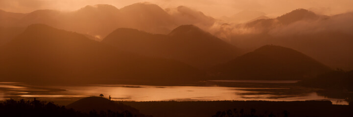 Silhouette of Mountains Above the Water under orange cloudscape clouds at sunset