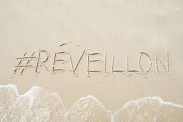 Hashtag social media message for Reveillon (New Year) written in smooth sand with a wave on the beach in Rio de Janeiro, Brazil