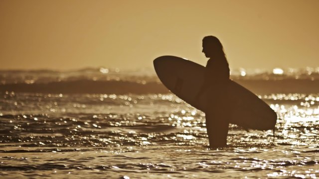 Footage of a surf girl walking into the ocean during a sunset. This is a slow motion shot (50FPS).