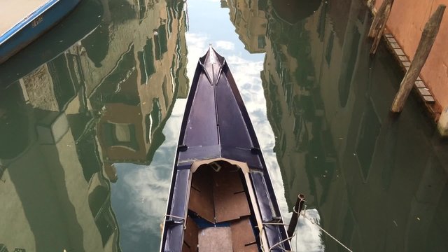 fragment of gondola with shaking reflections of Venice buildings in channel waters