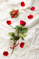 Rose, petals and strawberry on bed