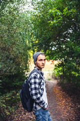 Naklejka na ściany i meble Portrait of young handsome man with backpack wanderer walk in the woods