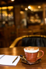 Hot latte art coffee cup on wooden table and note book