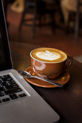 Hot art Latte Coffee in a cup and laptop on wooden table