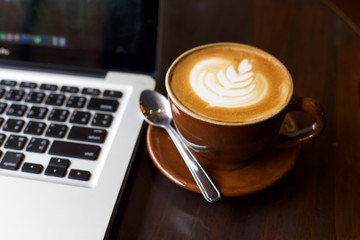 Hot art Latte Coffee in a cup and laptop on wooden table